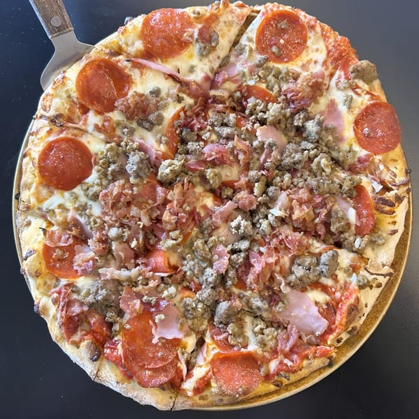 A whole meat lover's pizza from Sid's Pizza, topped with pepperoni, sausage, ham, and bacon.