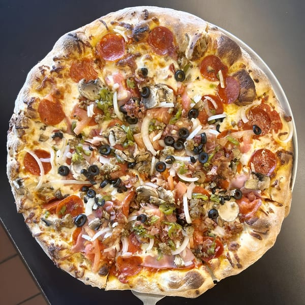 A whole Sid's Pizza with pepperoni, sausage, olives, onions, peppers, and mushrooms on a metal tray.
