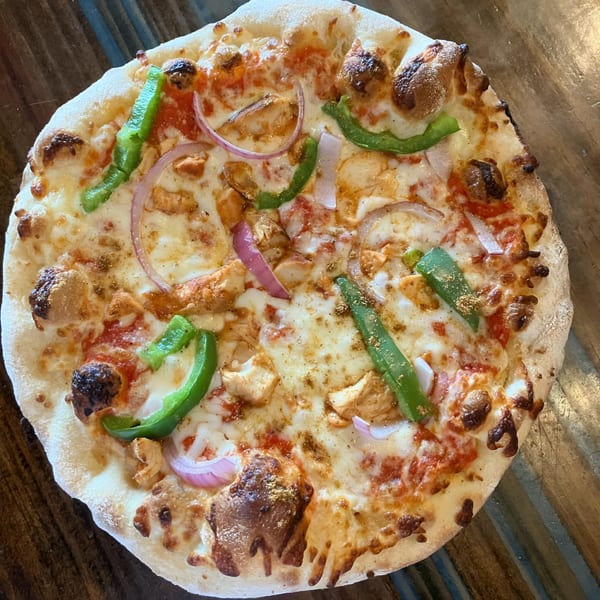 Sid's Pizza chicken pizza with green peppers, red onions, and melted cheese on a wooden table.