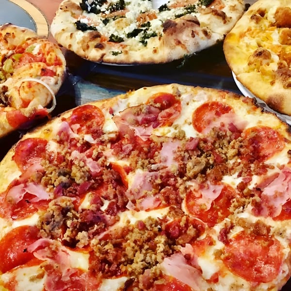 Four delicious Sid's Pizza pies, including pepperoni, sausage, ham, and white pizza, on a table.