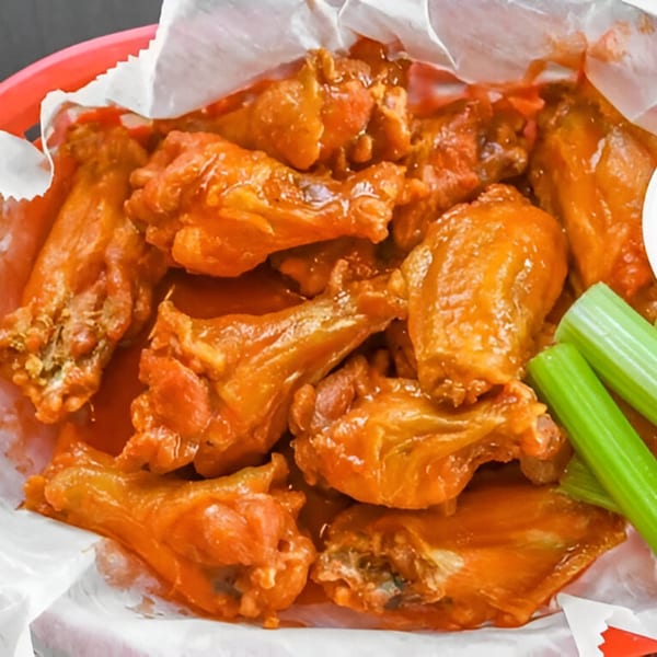 A basket of Sid's Pizza's buffalo wings, coated in orange sauce, with celery sticks.