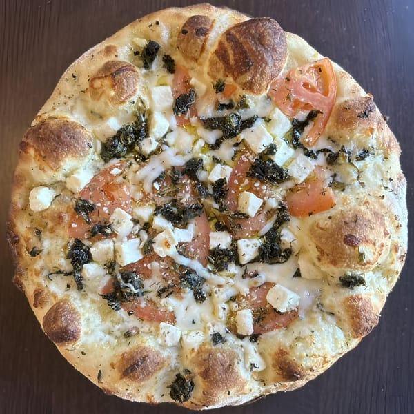 Sid's Pizza's white pizza with tomatoes, feta cheese, and herbs on a dark surface.