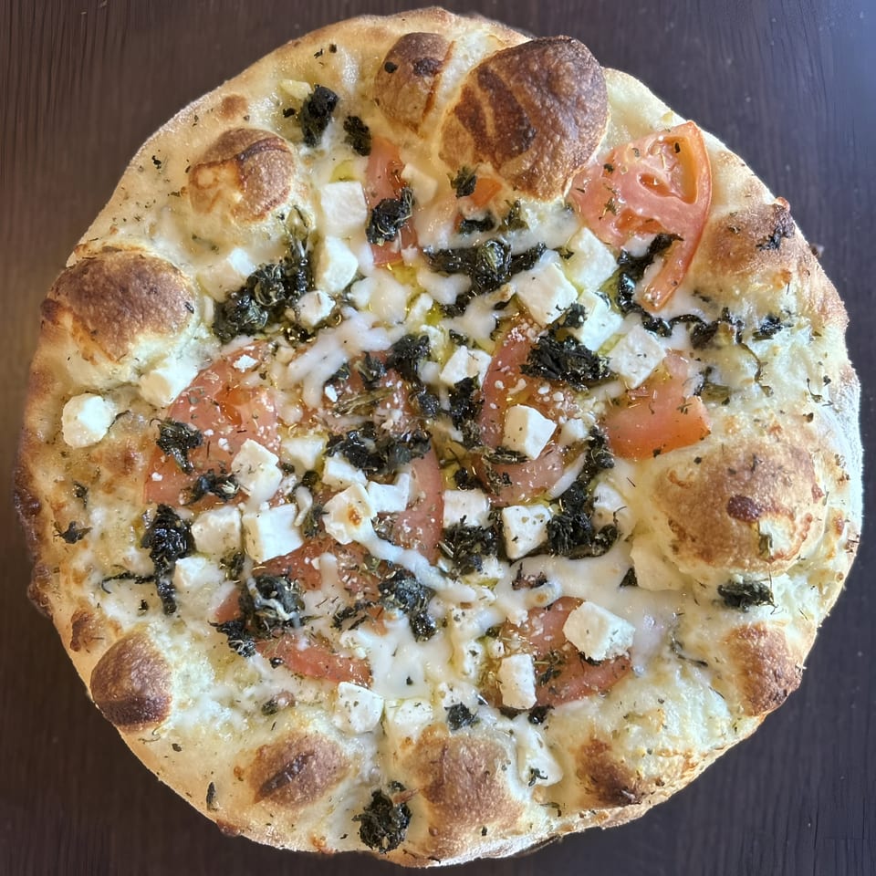 Sid's Pizza's white pizza with tomatoes, feta cheese, and herbs on a dark surface.