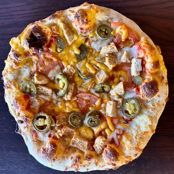 Sid's Pizza's chicken, tomato, and jalapeño pizza with melted cheese on a dark wooden surface.